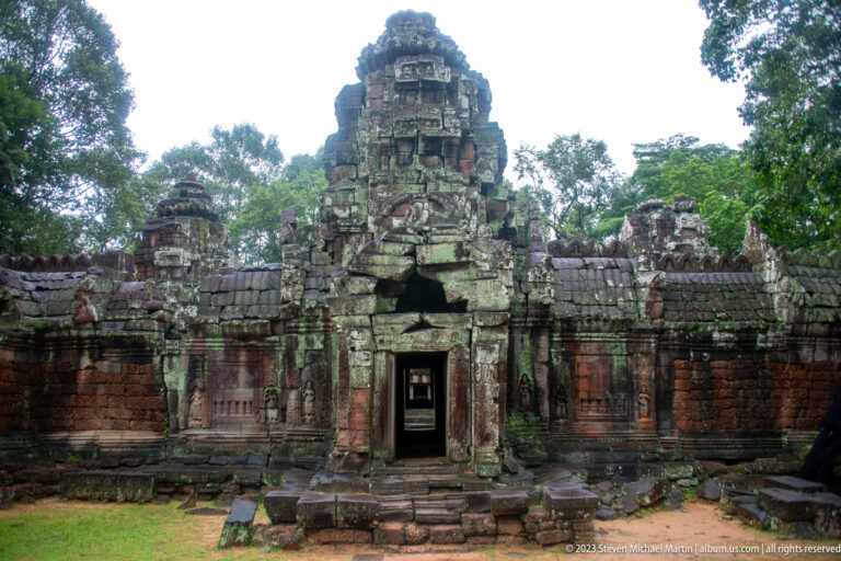 Frontal view of a central gateway tower with flanking walls, dark stone, and reddish masonry.