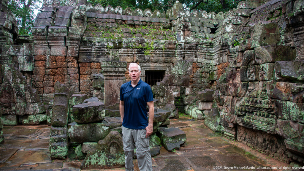 Visitor in a navy shirt standing among carved walls, doorways, and fallen stones at Ta Som.