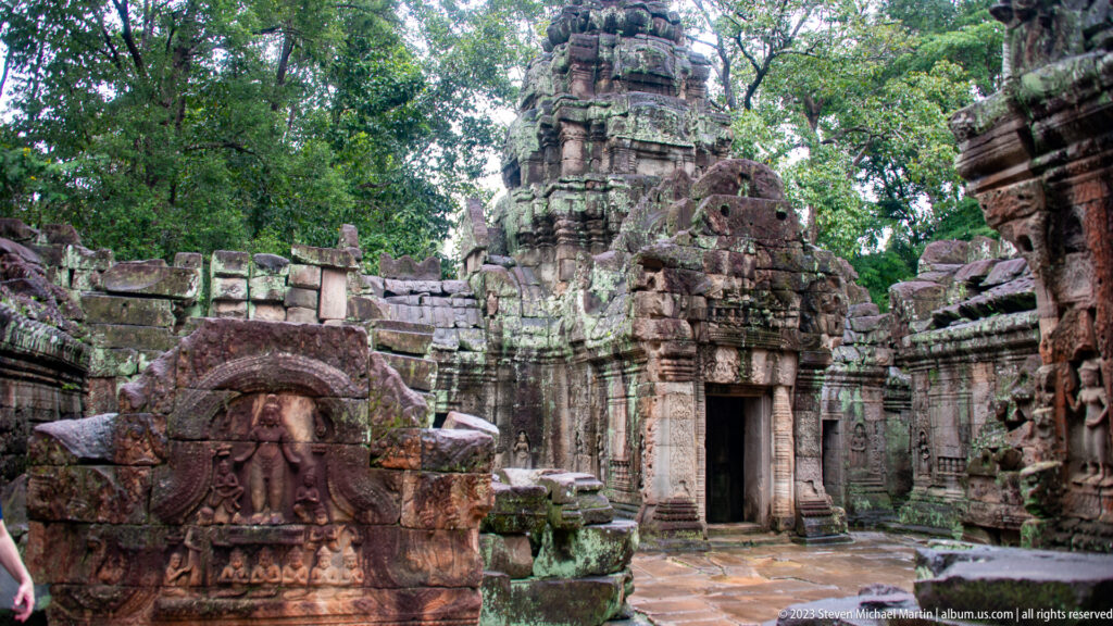 Oblique view of a towered sanctuary, doorway, broken walls, and carved stone block at Ta Som.