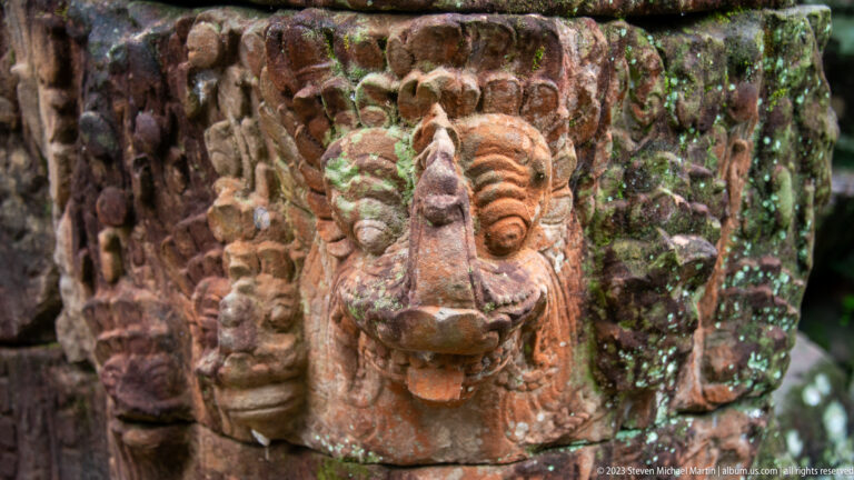 Close view of a projecting mythical animal head carved into reddish, weathered temple stone.