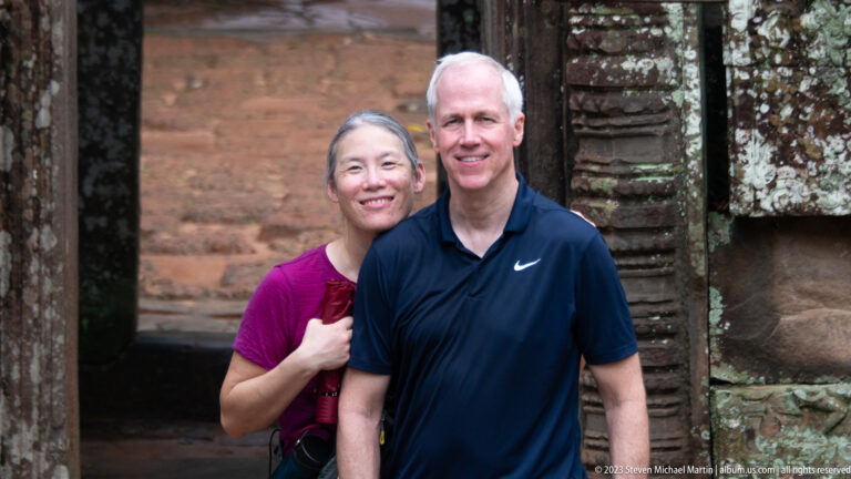 Two smiling visitors posing together within a weathered stone doorway at Ta Som.