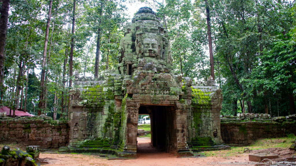 Frontal view of Ta Som’s face-tower gateway and open passage surrounded by forest and mossy walls.