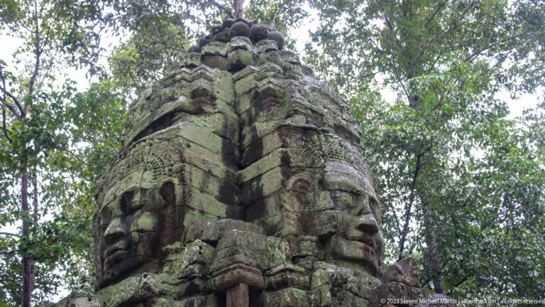Low-angle side view of a monumental carved face tower rising into the forest canopy.