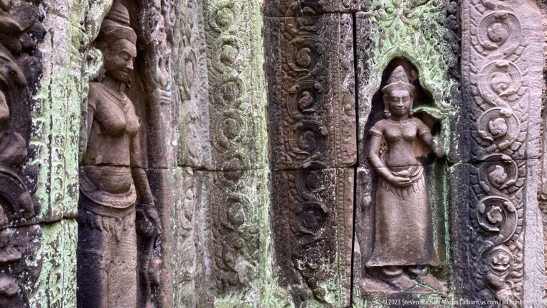 Oblique close view of carved female deities and ornate vertical doorway bands on weathered stone.