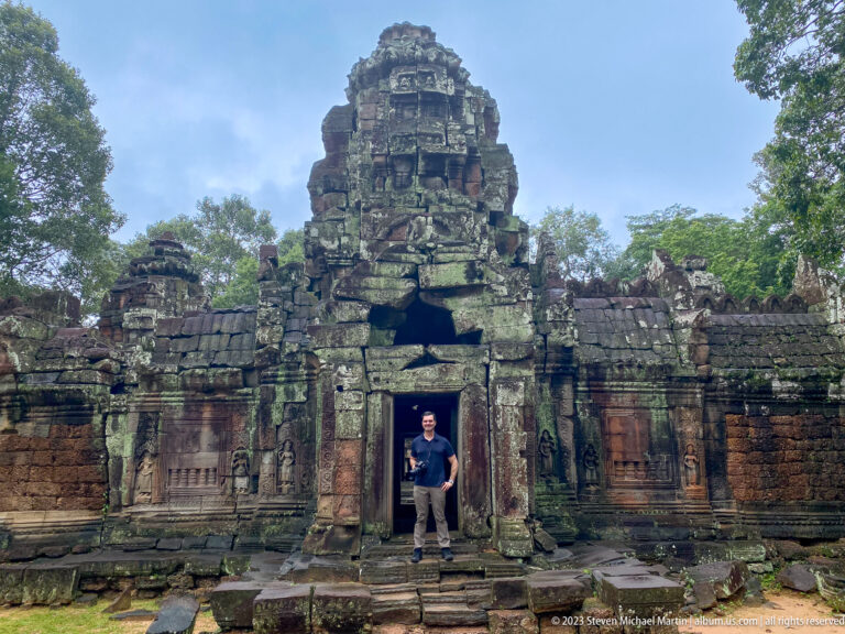Visitor standing in the central doorway of a towered Ta Som gateway with carved flanking walls.