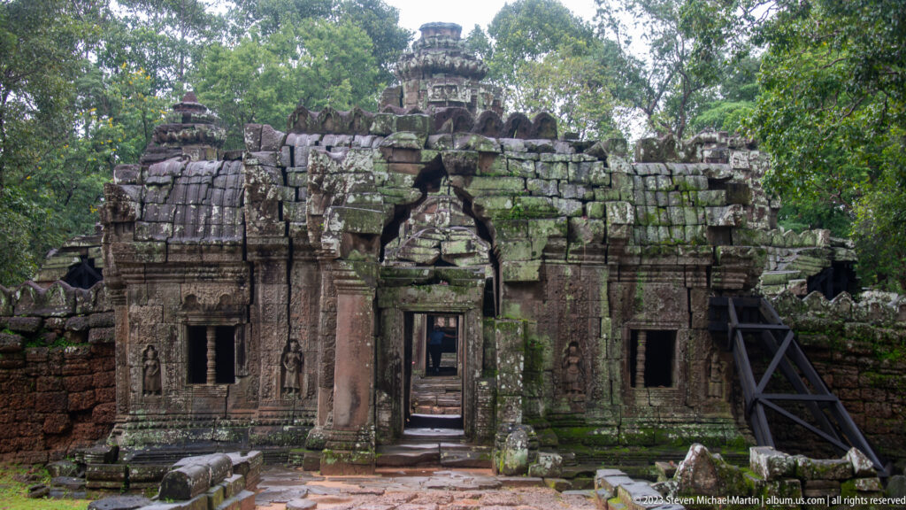 Ruined Ta Som gateway with a central doorway, side openings, fallen stones, and a support brace.