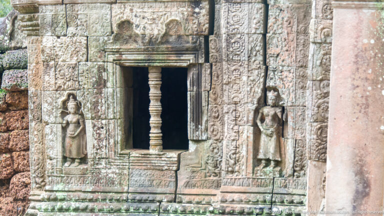 Stone window with a turned baluster, flanking female figures, and carved decorative bands.