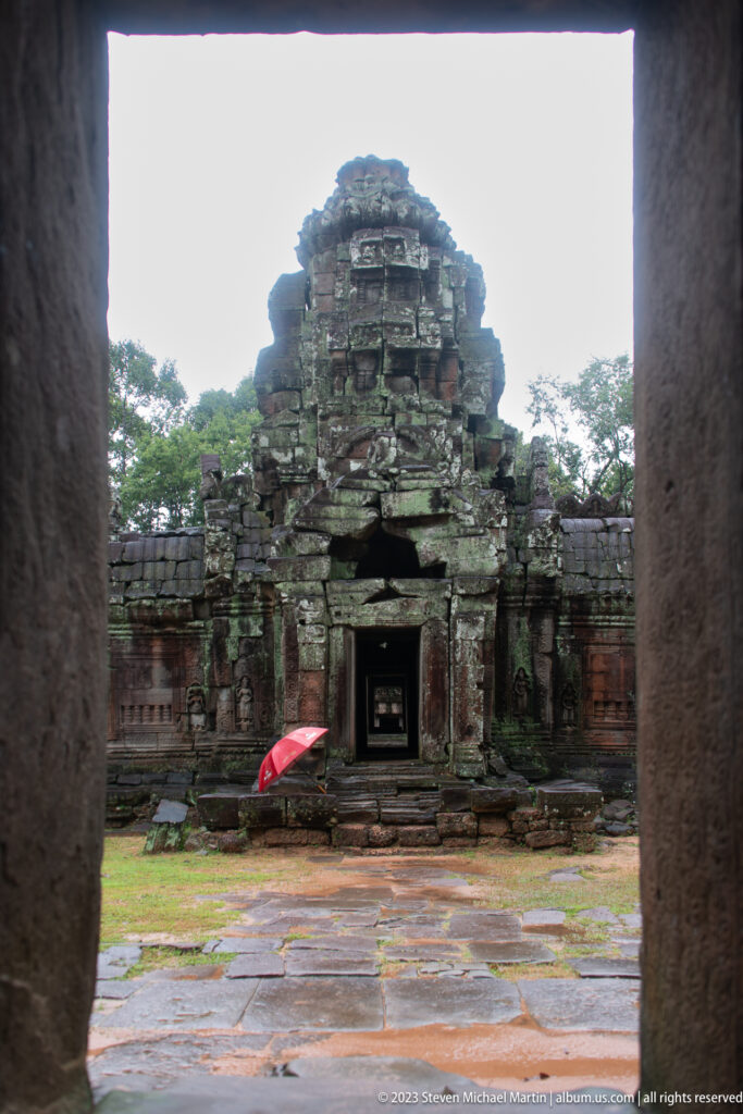 Dark doorway framing a ruined inner gateway across a wet stone courtyard at Ta Som.