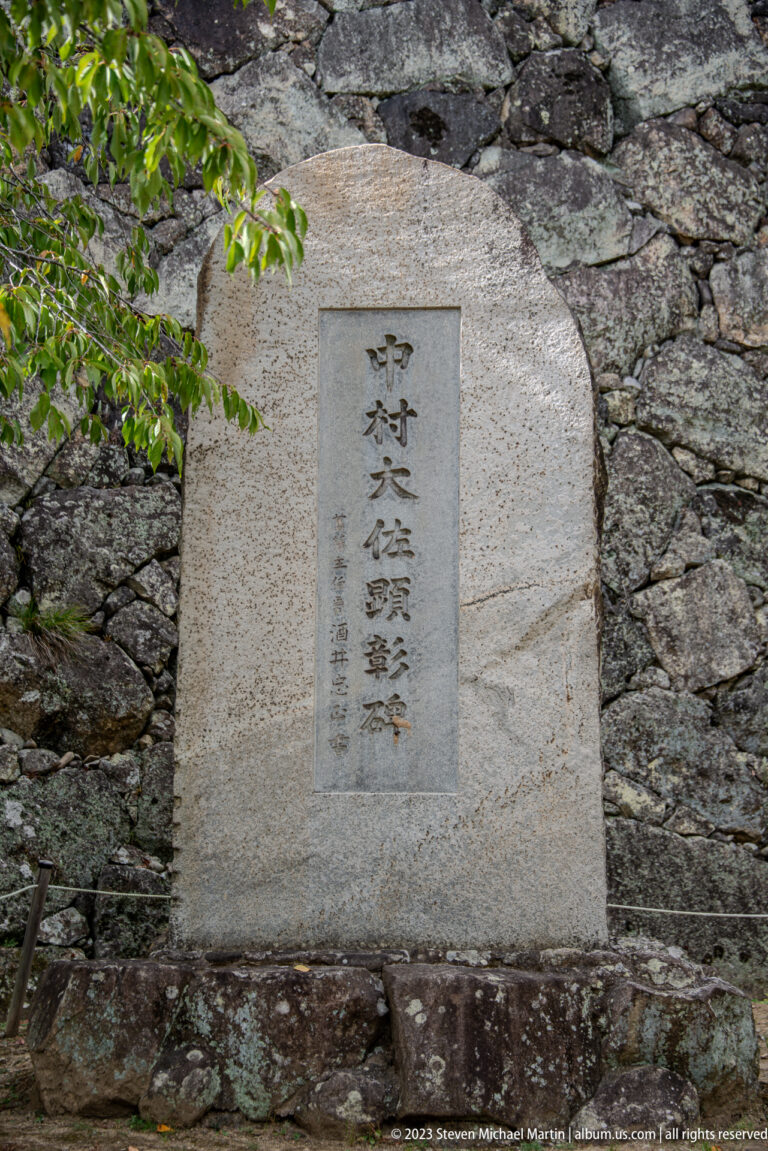 Vertical Japanese inscription carved on a rectangular stone plaque set into a rough castle wall.