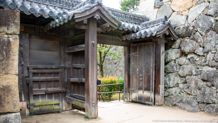 Wooden gate with tiled roof set between large stone walls at Himeji Castle.