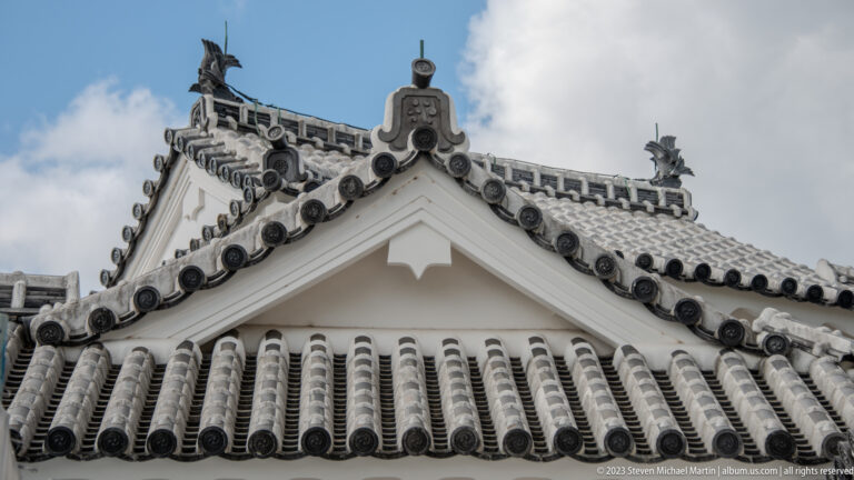 Close view of a white gable with gray ceramic roof tiles and ridge ornament.