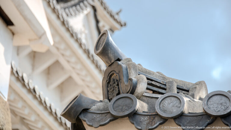 Close-up of ceramic roof finial and ridge tiles against the sky.