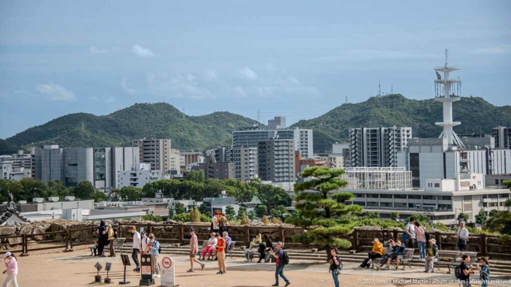 Visitors overlooking the city from Himeji Castle with mountains in the background.