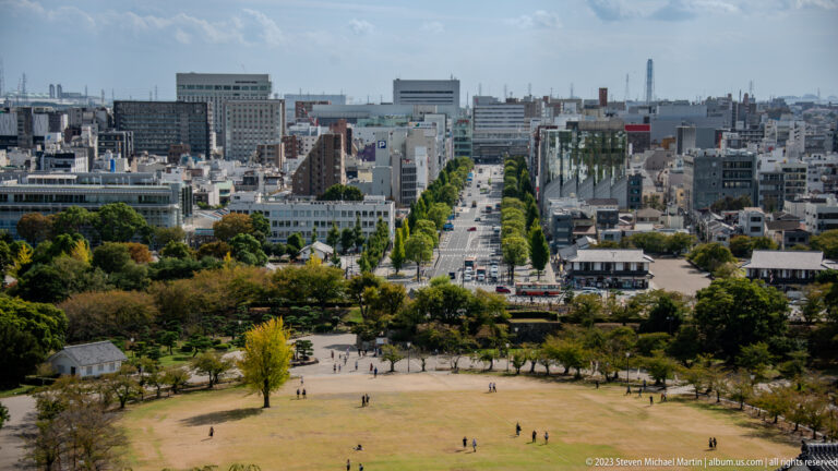 Panoramic city view from Himeji Castle over parks and streets.