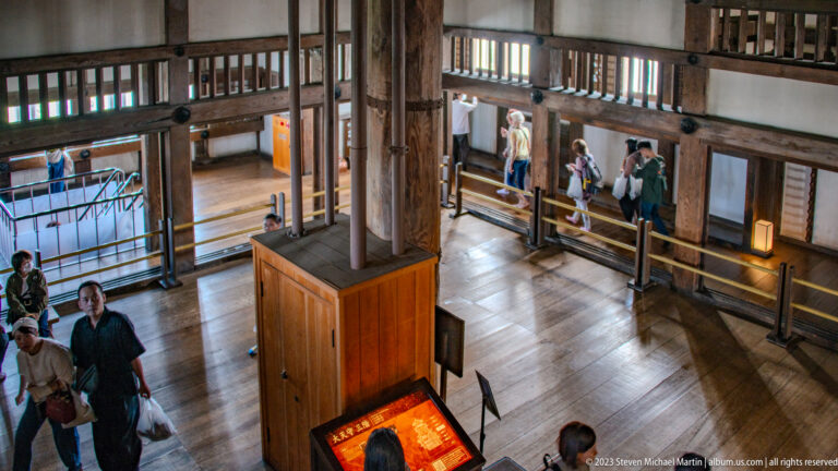 Open timber hall inside Himeji Castle with visitors.