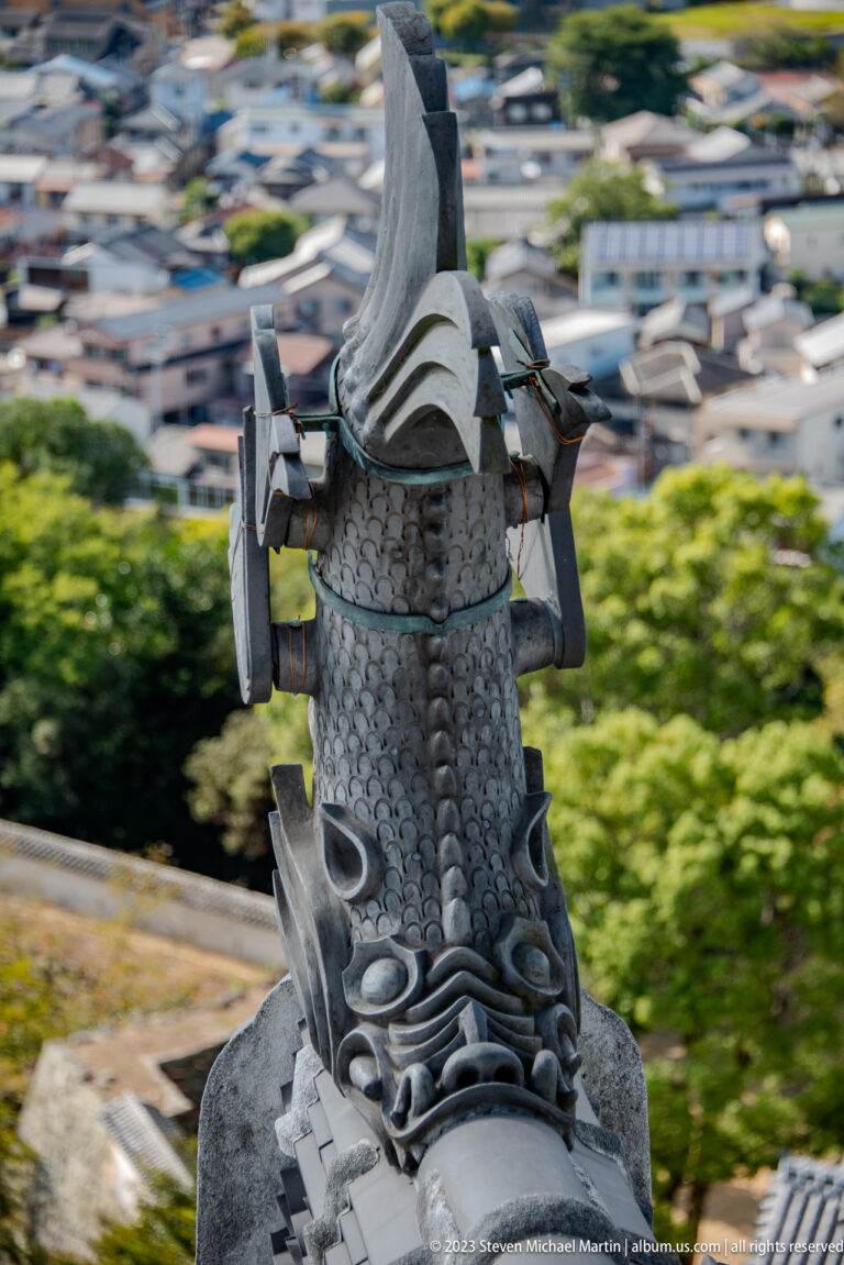 Dark ceramic shachihoko roof ornament with an upturned tail overlooking the city of Himeji.
