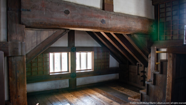 Heavy timber beams, diagonal braces, windows, and a steep stair inside Himeji Castle.