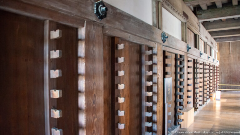 Repeating timber posts and horizontal wall framing along a wooden gallery inside Himeji Castle.