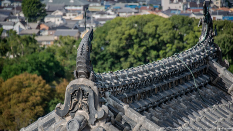Curved tiled roof ridge ending in a shachihoko ornament above the city.