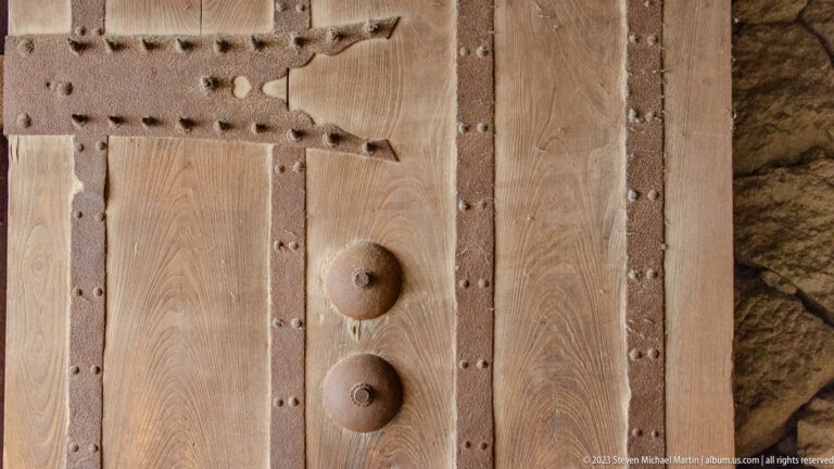 Close view of a reinforced wooden castle door with iron straps and bosses.