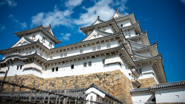 Main keep rising above stone ramparts under blue sky.