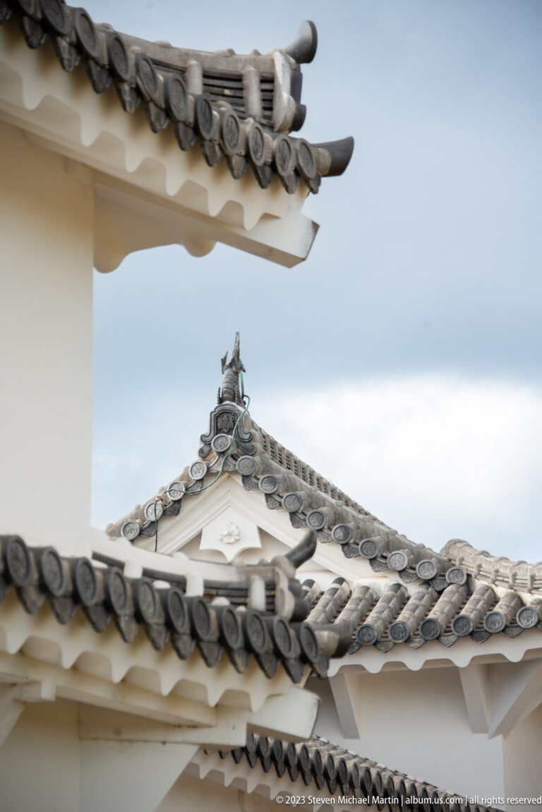 Overlapping gray-tiled roofs and white gables at Himeji Castle beneath an overcast sky.