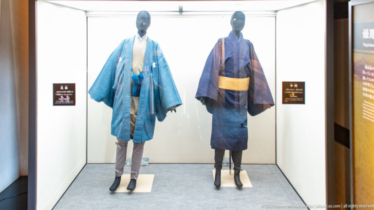 Two blue historical Japanese garments displayed on mannequins inside a museum case.