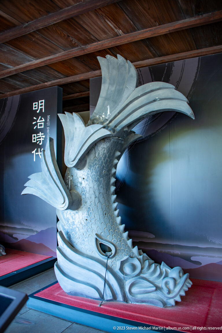 Large silver-gray shachihoko roof ornament with scaled body, dragonlike head, and raised tail.
