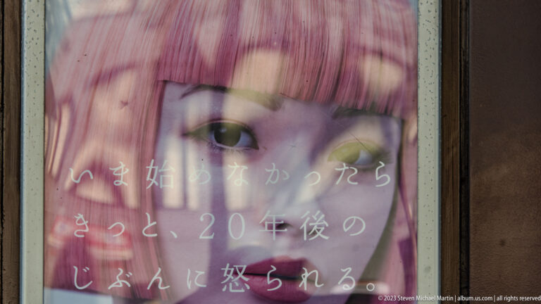 Close-up of a woman's face on a Japanese advertisement behind reflective glass, with white Japanese text printed across the image.