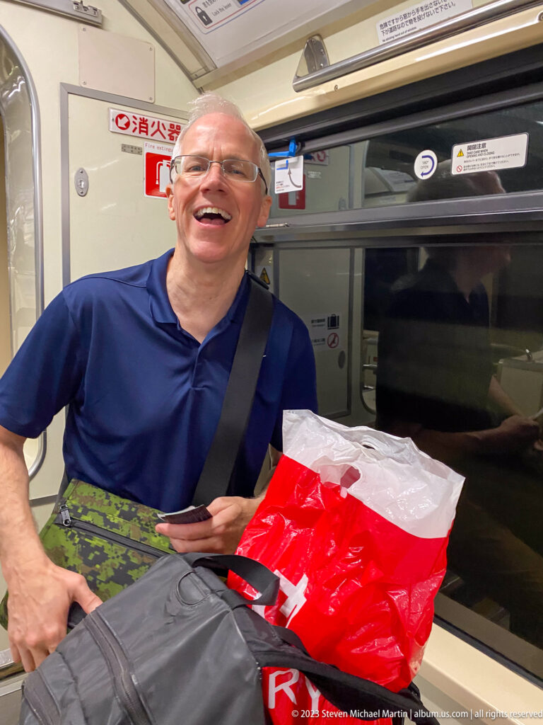 Smiling traveler seated with luggage beside a window inside a Japanese Shinkansen train.