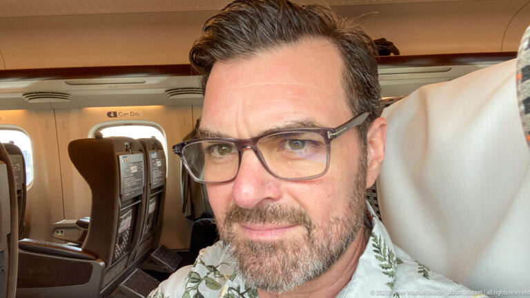 Close portrait of a bespectacled traveler seated inside a Shinkansen carriage.