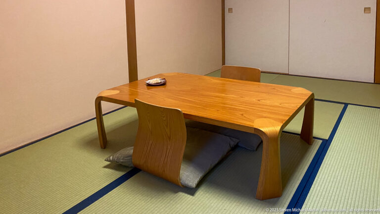 Japanese tatami room with a low wooden table, two floor chairs, cushions, and sliding panels.