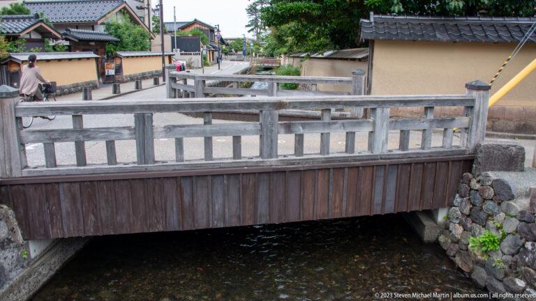 Weathered wooden bridge crossing a narrow canal between stone walls and plaster boundaries.