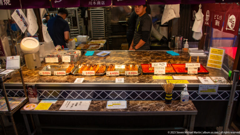 Large crabs displayed across a market counter with price cards and a vendor behind.