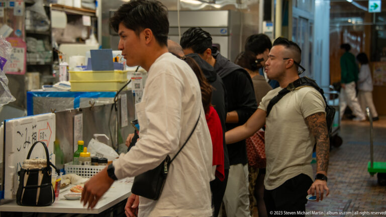 Workers and shoppers moving through a narrow aisle beside a seafood counter in Omicho Market.