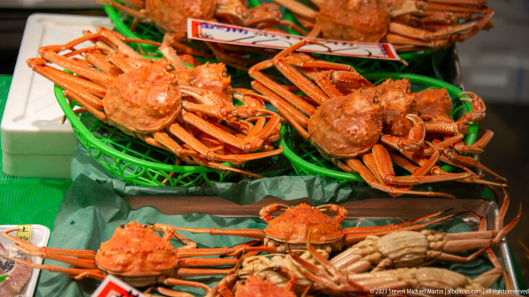 Large orange-red crabs stacked in green trays at a seafood market counter.