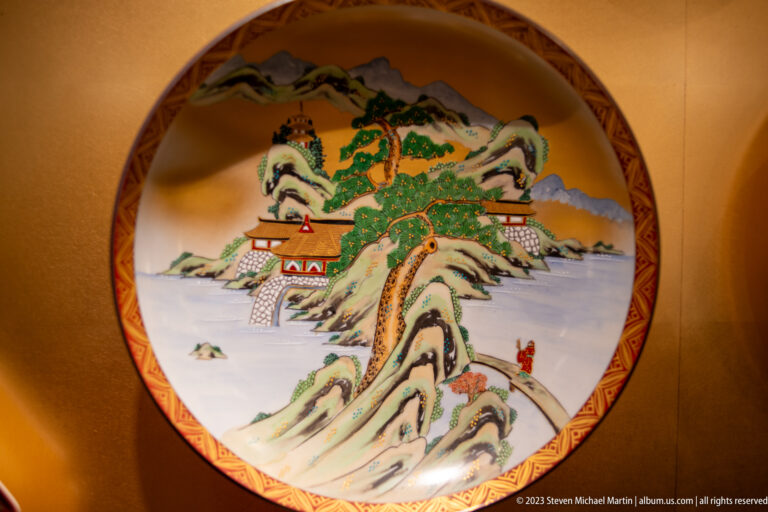 Large porcelain charger painted with a castle complex among mountains, pine trees, clouds, and water.