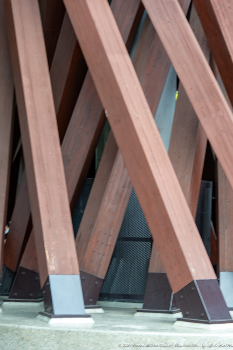 Close-up of intersecting reddish timber braces with metal-clad feet at the base of the Tsuzumi-mon Gate.