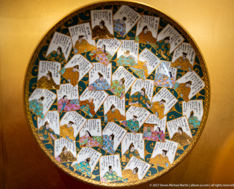Porcelain charger covered with overlapping Japanese calligraphy and illustrated poetry-style cards.