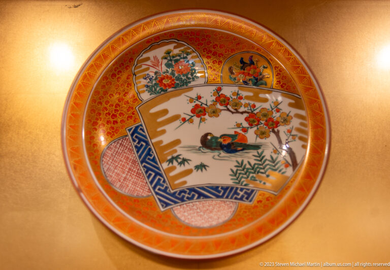 Orange-red porcelain charger divided into floral, figural, geometric, and textile-patterned sections.