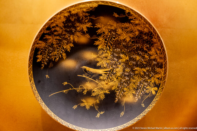 Round black decorative panel with gold foliage and two pale birds, set in a gold-toned surround.