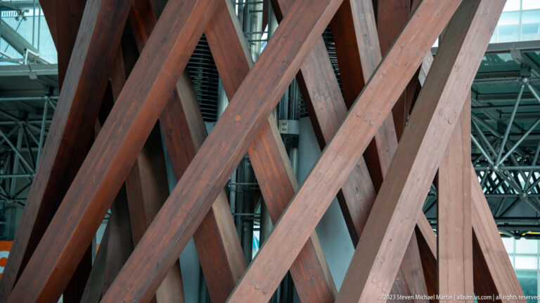 Layered X-shaped timber braces of the Tsuzumi-mon Gate with station structure visible through the gaps.