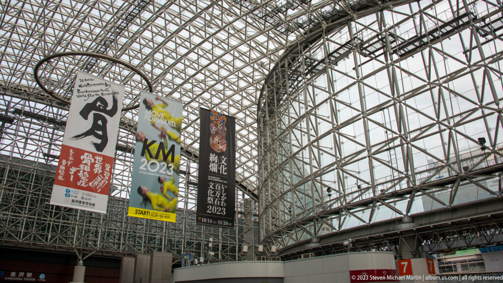 Event banners suspended beneath the curved steel-and-glass Motenashi Dome inside Kanazawa Station.