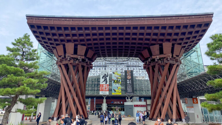 Front view of Kanazawa Station’s Tsuzumi-mon Gate with massive timber columns and travelers below.