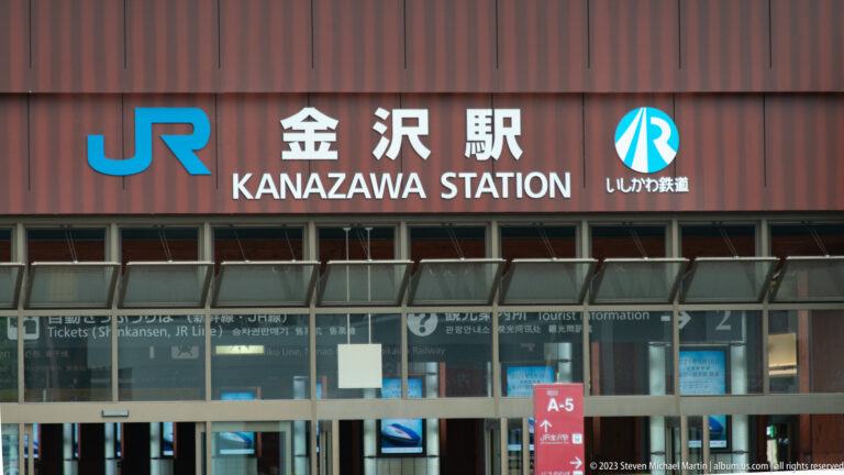 Kanazawa Station sign in Japanese and English above glass doors with JR and IR railway logos.