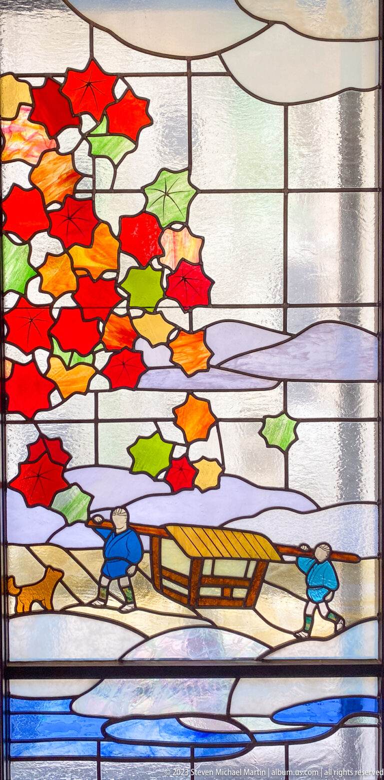 Stained-glass winter landscape with figures on a bridge, blue water, and red leaves.
