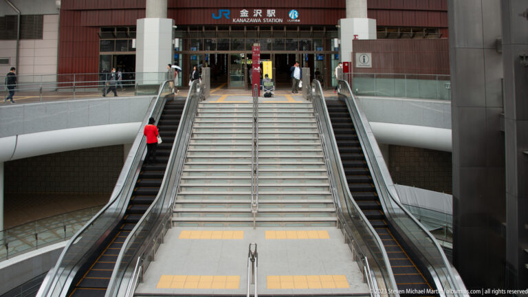 Wide staircase between escalators leading to the signed entrance of Kanazawa Station.