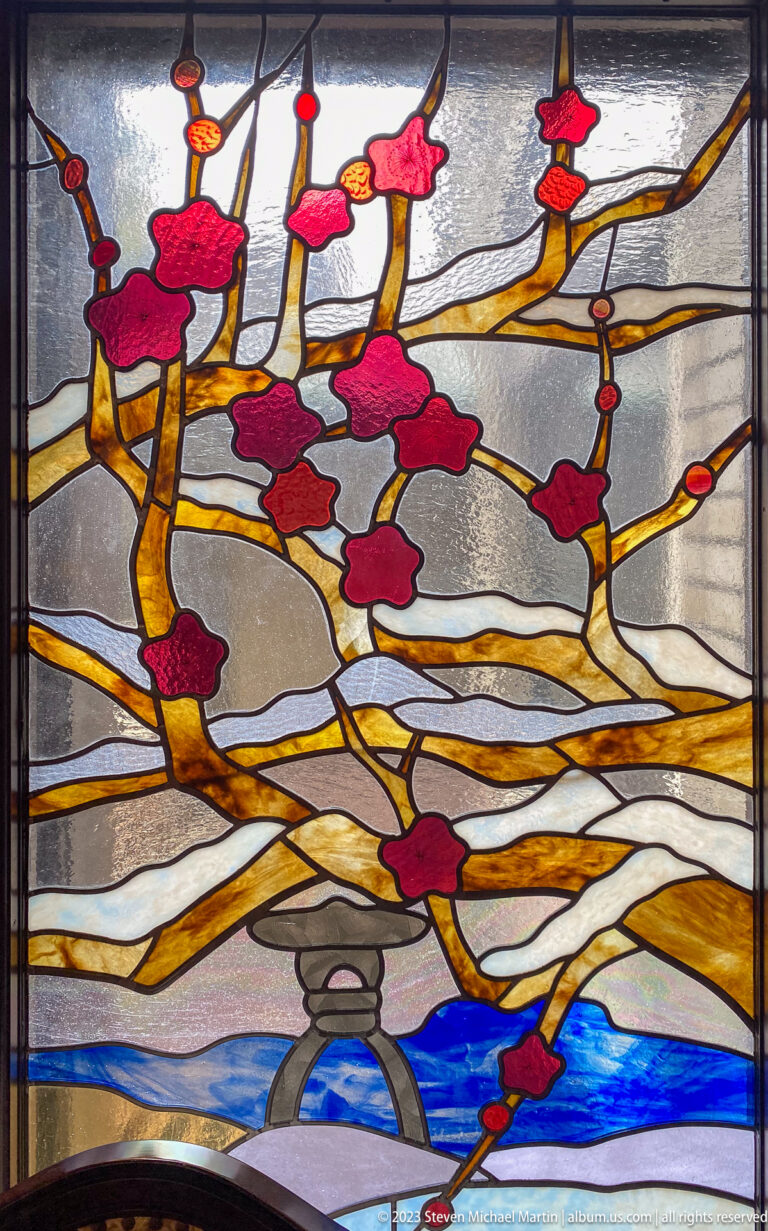 Stained-glass detail of red flowering branches above blue water and a gray arched feature.