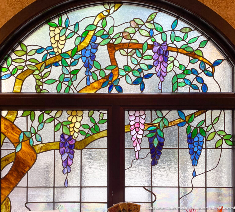 Close frontal view of an arched stained-glass grapevine window divided by dark timber framing.