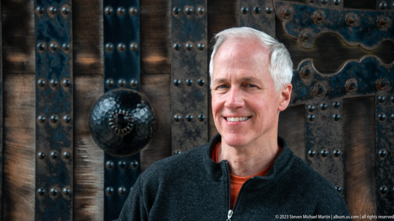 Smiling visitor standing before a massive wooden castle door with iron straps and rivets.
